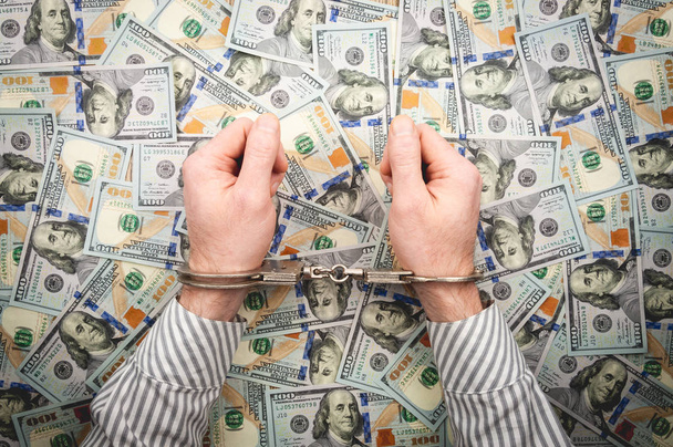 Men's hands in handcuffs on the background of dollar bills. - Fotografie, Obrázek
