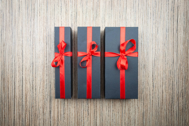 Three black gift boxes with a bow on a wooden table - 写真・画像