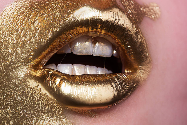 Golden girl. Paint golden on woman face. Provocative makeup. Glamorous life. Expensive cosmetics. Rich woman. Gold concept. Mat lips, white teeth. Makeup artist concept. Beauty saloon. Fashion show. - 写真・画像