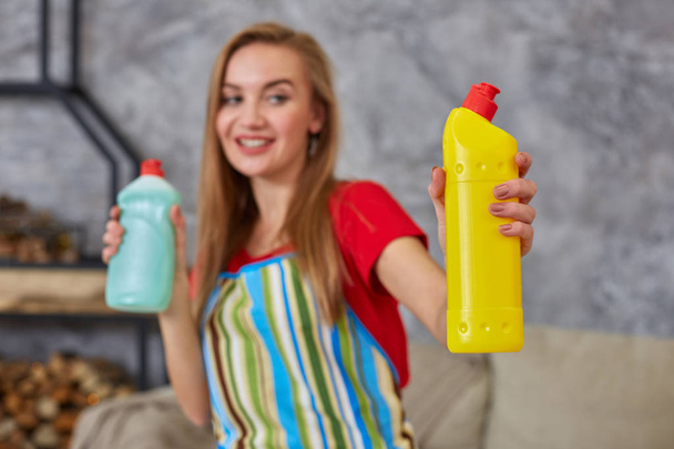 Nő összehasonlít két tisztítószer üveg otthon takarítás nappaliban. Otthoni munka. - Fotó, kép