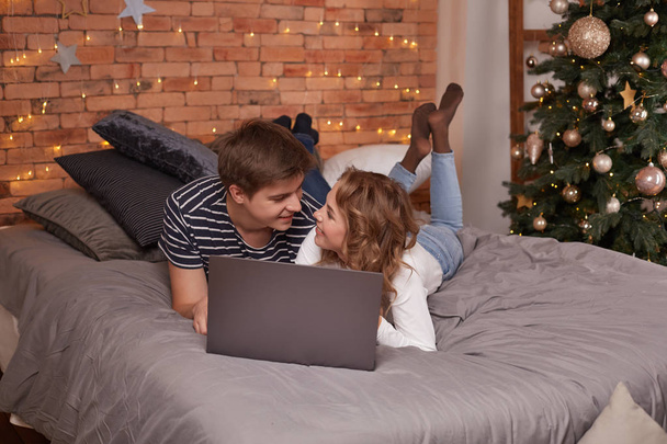 Smiling young couple man and woman lying in bed with laptop and looking at each other - Photo, Image