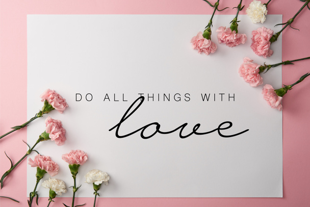top view of pink and white carnation flowers and card with do all things with love lettering on pink background - Fotografie, Obrázek