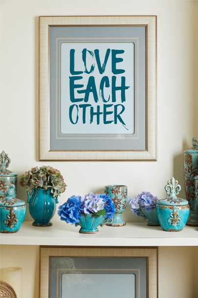 picture frame with love each other lettering and turquoise ceramic ornate vintage vases with flowers on shelf - Foto, afbeelding