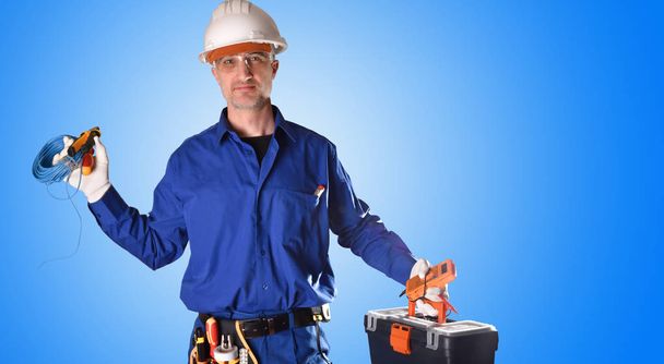 Uniformed electrician in blue overalls and safety protections and tools on blue gradient background isolated Front view. - Photo, Image