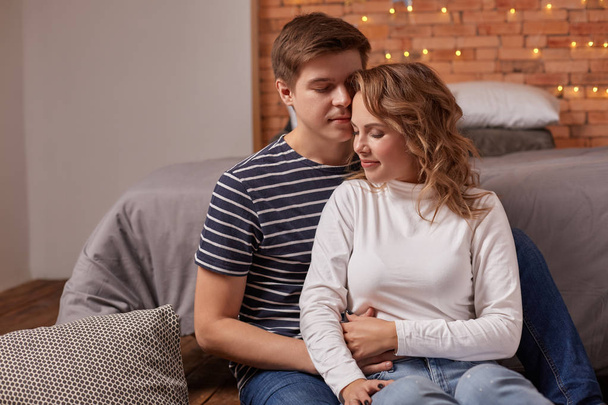 Retrato de um jovem casal amoroso descansando em um sofá cinza juntos em casa e abraçando
 - Foto, Imagem