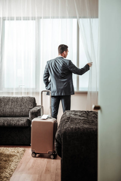 Businessman standing near his luggage looking into window - Foto, Bild
