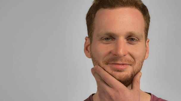 caucasian guy with red hair posing scratching his beard handsome redhead men wearing in casual t-shirt. Portrait hipster young caucasian man on grey background - Photo, Image