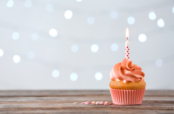 Delicious orange cupcake with burning candle on table against blurred background. Space for text  - Foto, afbeelding