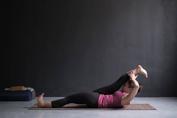 Женщина делает Yoga asana Supta padangusthasana или наклоняя руку к большой позе пальца ноги
 - Фото, изображение