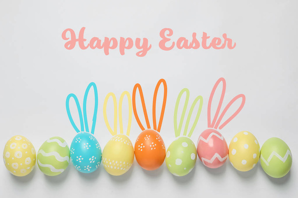 Set of colorful eggs with bunny ears on light background, top view. Happy Easter - Foto, Imagem