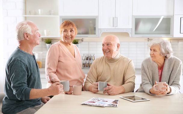Elderly people spending time together at table in kitchen - Foto, imagen
