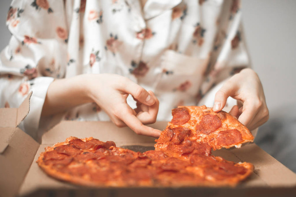 Close-up van vrouwen handen Neem een stukje pizza uit de kist. Meisje in een pyjama neemt een stuk van hete verse pizza van de levering. - Foto, afbeelding