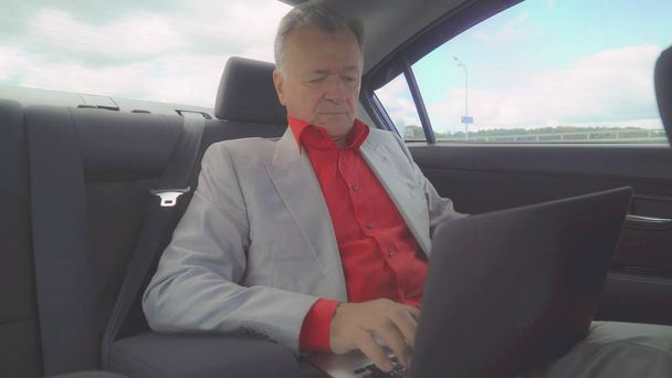 Uomo di mezza età che utilizza il computer portatile in macchina si siede sul sedile posteriore
. - Foto, immagini