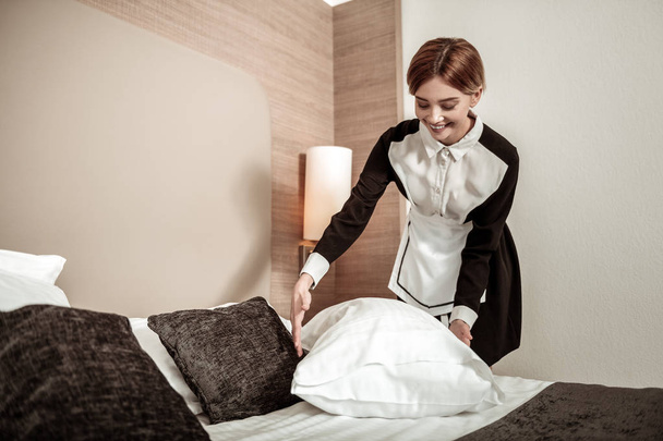 Bionda cameriera d'albergo sorridente mentre fa il letto dei clienti
 - Foto, immagini