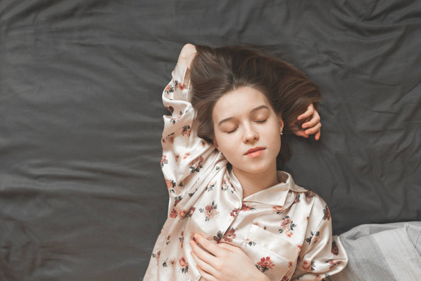 Portrait of a young girl in a pajama sleeping on the bed top view. Attractive girl resting on the bed with a view from above. Woman lies on the bed with her eyes closed. Copyspace - Photo, Image