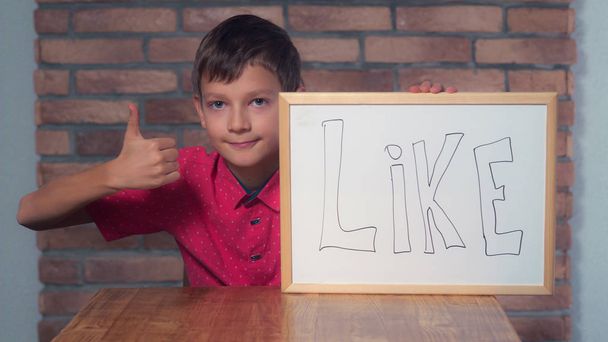 παιδί κάθεται στο γραφείο κρατώντας πινακάκι με γράμματα όπως  - Φωτογραφία, εικόνα