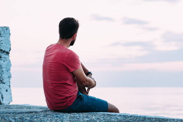Молодий чоловік насолоджується синьою годиною біля моря
 - Фото, зображення