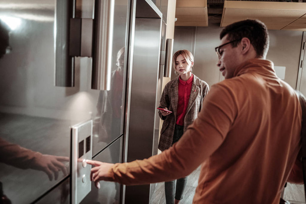 Calling the elevator. Dark-haired man wearing orange polo neck calling the elevator standing near his girlfriend - Photo, Image