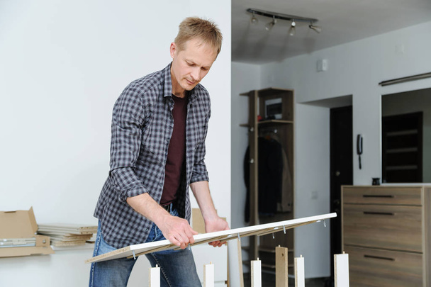 The man assembles the furniture at home. He sets the sidewall of the chest of drawers. - Foto, Bild