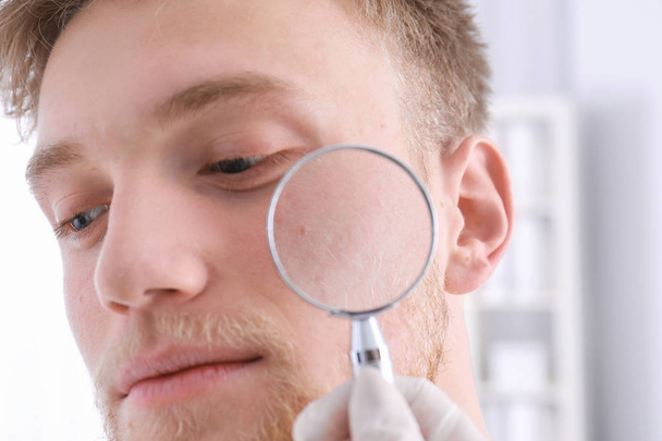 Dermatologist examining patient with magnifying glass in clinic, closeup view - Valokuva, kuva