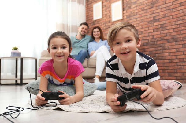 Cute children playing video games while parents resting on sofa at home - Photo, image