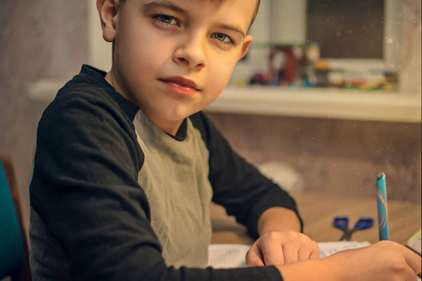 Nuori poika istuu pöydässä tekemässä koulun läksyjä.
 - Valokuva, kuva