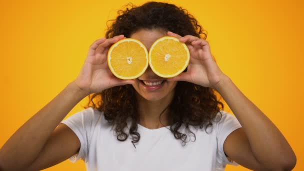 Cheerful curly-haired girl putting orange slices on eyes and smiling, vitamin c - Materiaali, video