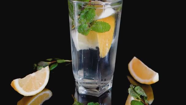 Sparkling cocktail with slices of lemon, ice cubes and mint on a dark background. - Footage, Video