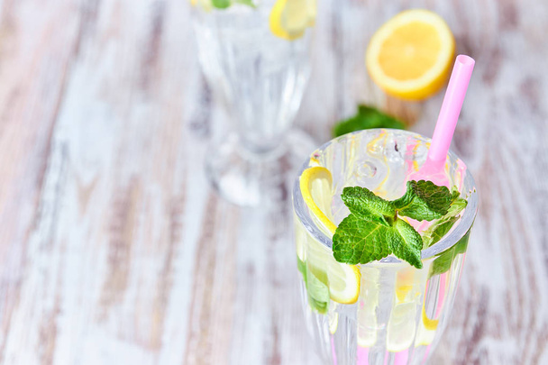 Lemonade with ice, lemon slices and mint in a glass with straw on a light wooden background. copy space. summer, refreshing drink. - Photo, image