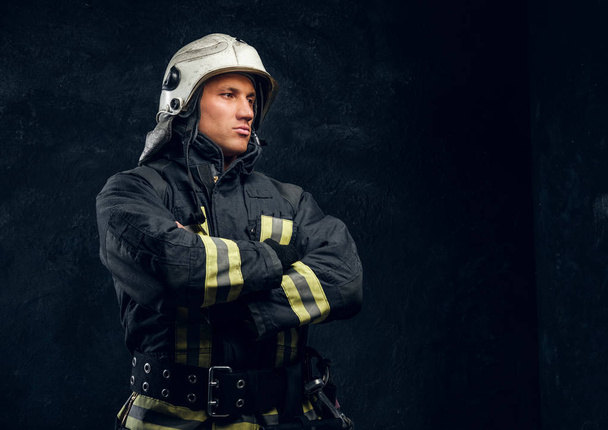 Ritratto di pompiere in uniforme e cavalletti a casco con le mani incrociate, guardando lateralmente con uno sguardo sicuro
. - Foto, immagini