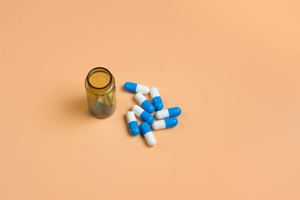 Niebieskie i białe tabletki w brązowej szklanej butelce na pomarańczowym tle. Kopiować miejsca na tekst - Zdjęcie, obraz
