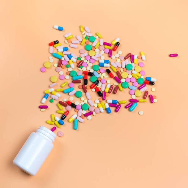 Colored pills, tablets and white bottle on orenge background. Copy space for text - Фото, зображення