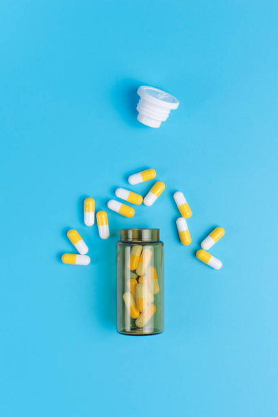 Medycyna białe i żółte pigułki lub tabletki upuść z brązowego szkła butelki na niebieskim tle - Zdjęcie, obraz