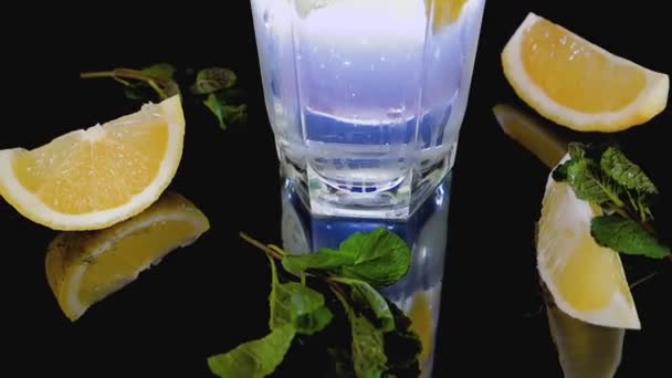 Sparkling cocktail with slices of lemon, ice cubes and mint on a dark background - Footage, Video