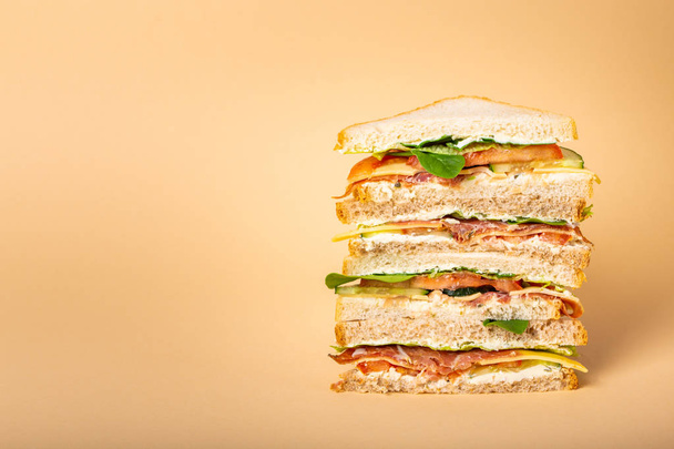 Close up of tall cut tasty sandwich with cheese, ham, prosciutto, fresh lettuce, tomatoes, cucumbers on pastel yellow background. Healthy gourmet sandwich for breakfast or lunch. Space for text  - Fotografie, Obrázek