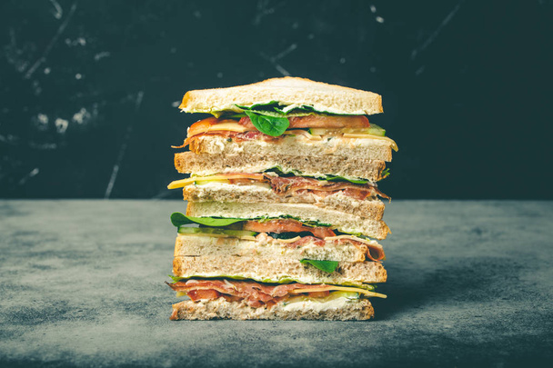 крупним планом смачний бутерброд з сиром, шинкою, прошутто, свіжим салатом, помідорами, огірками на сірому фоні сільського каменю. Здоровий бутерброд для гурманів на сніданок або обід, концепція
 - Фото, зображення