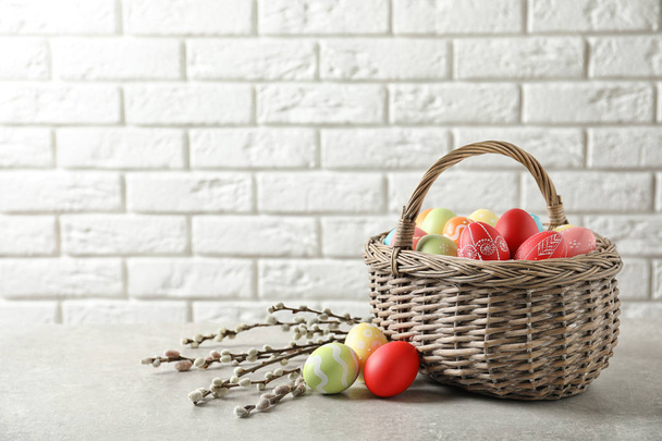 Wicker basket with colorful painted Easter eggs on table near brick wall, space for text - Фото, зображення