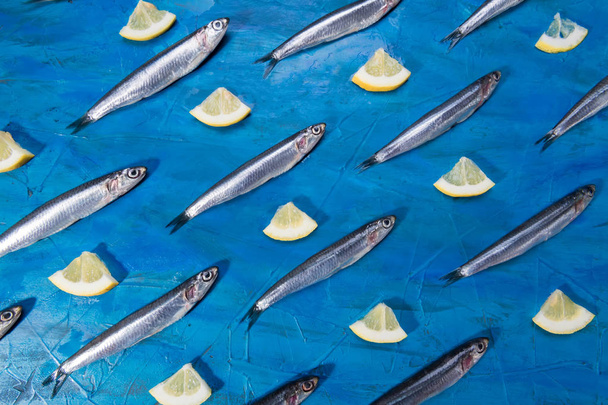 Vis patroon. Ansjovis met schijfje citroen op een zwarte steen op een achtergrond van de blauwe zee. Vis gevangen in de Ionische zee - Foto, afbeelding