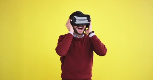 Man wearing a virtual reality glasses in a studio with a yellow background wall and exploring the virtual world very excited - Video, Çekim