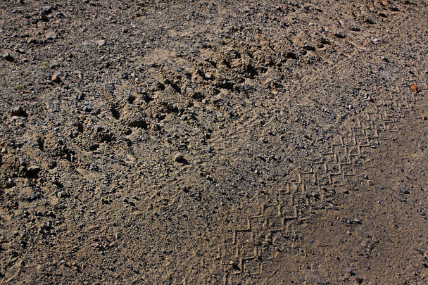 A pista do trator da lagarta numa estrada de terra. A trilha corre diagonalmente
 - Foto, Imagem