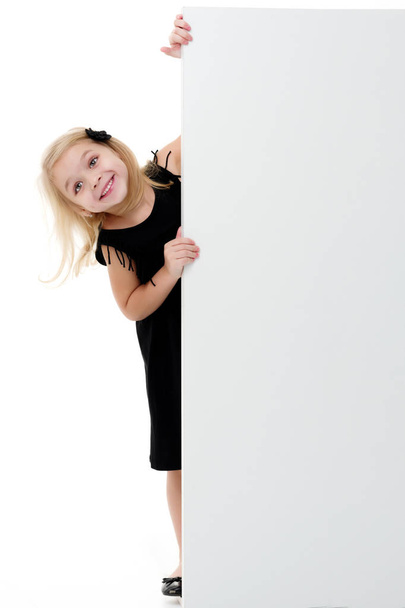 A little girl is looking from behind an empty banner. - Foto, Imagen