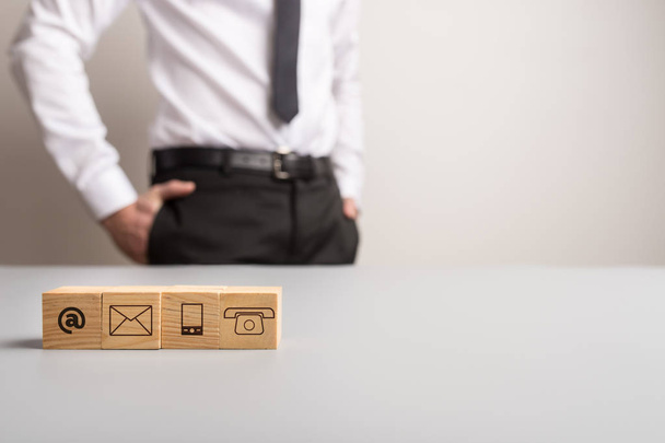 Símbolos de comunicación en bloques de madera con hombre de negocios de pie en el fondo y espacio de copia en el lado derecho de una imagen
. - Foto, imagen