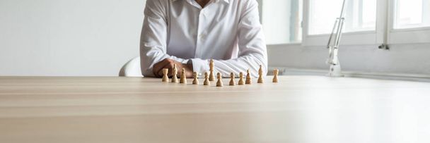 Imagem ampla do executivo de negócios sentado em sua mesa com peças de xadrez posicionadas na frente dele em uma imagem conceitual
 - Foto, Imagem