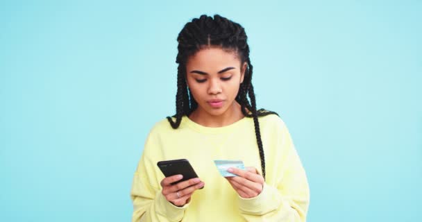 African pretty lady using a credit card and make a online order with her smartphone on a blue background wall. - Кадры, видео