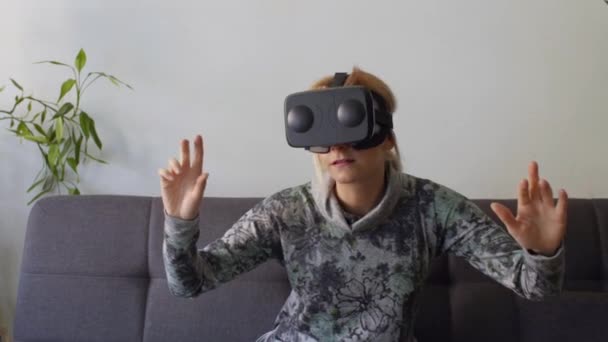 woman at home enjoying virtual reality goggles on sofaLooking around and using gestures with hands - Filmmaterial, Video