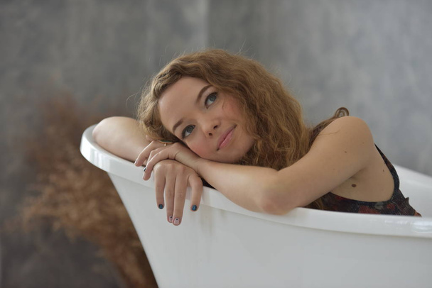 νεαρή γυναίκα τοποθέτηση σε bathtub.relaxed χρόνο σε bathroom.young γυναίκα χαλαρώνοντας στην μπανιέρα. Όμορφη γυναίκα με ένα γλυκό χαμόγελο. Σε μια υπέροχη στάση σε μια χαλαρωτική μέρα - Φωτογραφία, εικόνα