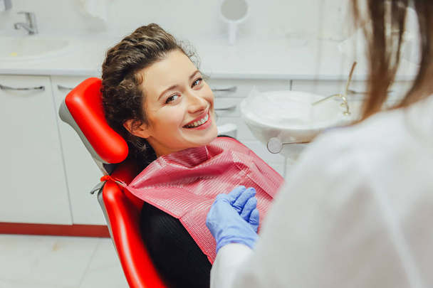 Woman at the reception of a dentist in a dental clinic. She sits in a red chair. Happy patient and dentist concept - Фото, изображение