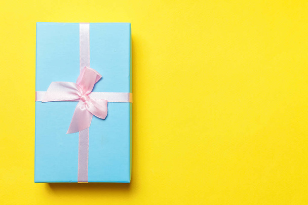 Christmas New Year birthday valentine celebration present romantic concept. Gift box wrapped blue paper isolated on yellow colourful trendy modern fashion background. Flat lay top view copy space - Photo, Image