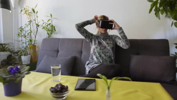 woman at home enjoying virtual reality goggles on sofaLooking around and using gestures with hands - Filmmaterial, Video