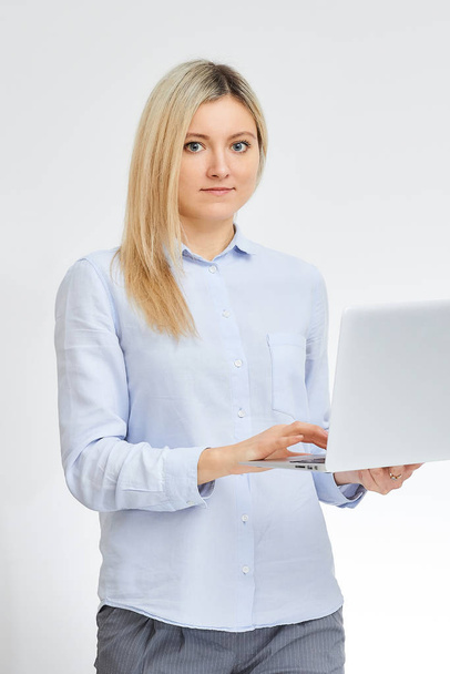 Jovem loira caucasiana mulher fica de lado segurando seu computador caderno de alumínio no escritório com um fundo branco
. - Foto, Imagem